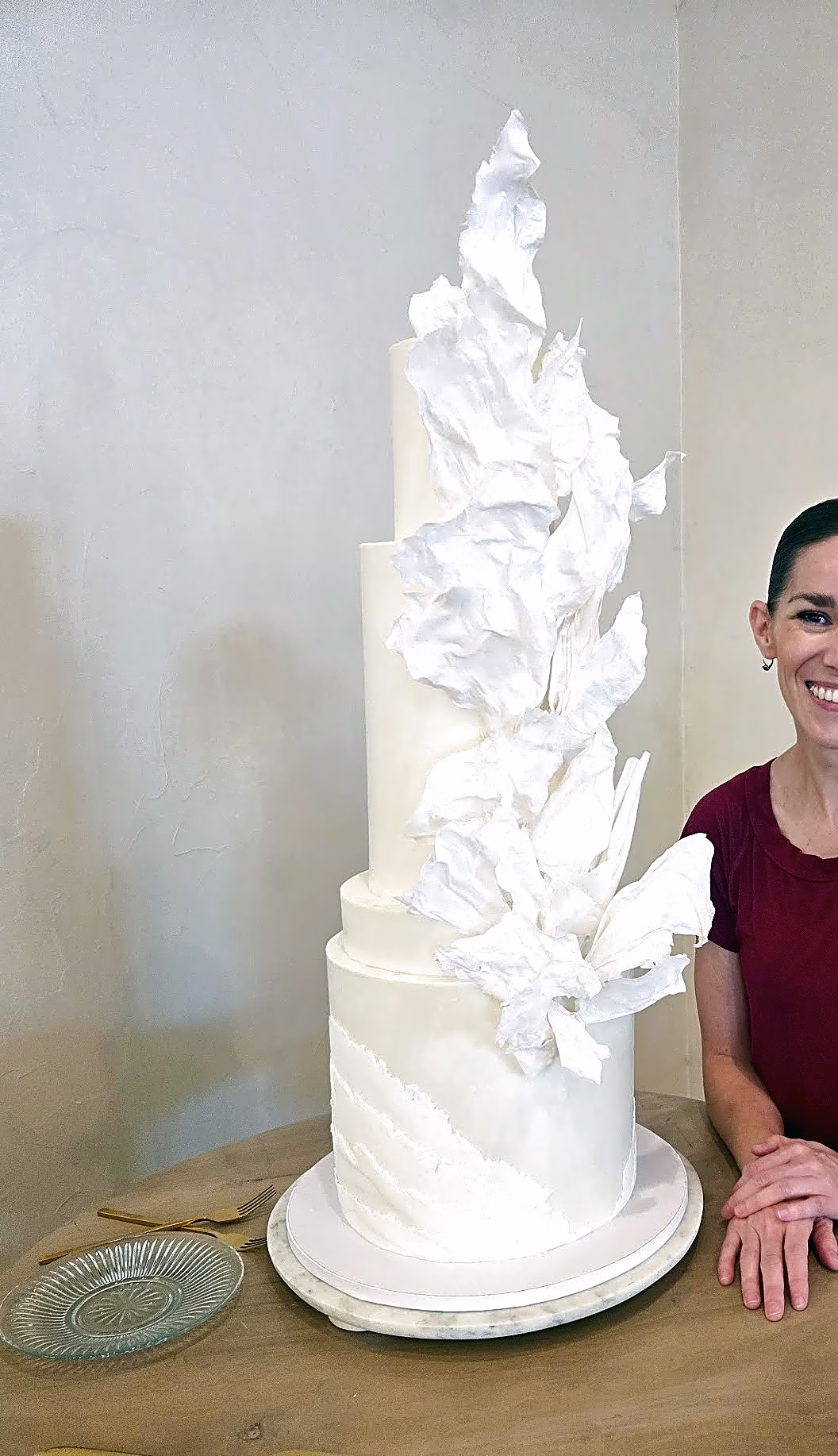 Tall white wedding cake with wafer paper sails climbing the tiers, beside cake artist Erika Ellis